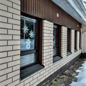 Vaalea tiilirakennus sivusta, ikkunoissa paperista askarteltuja lumihiutaleita.