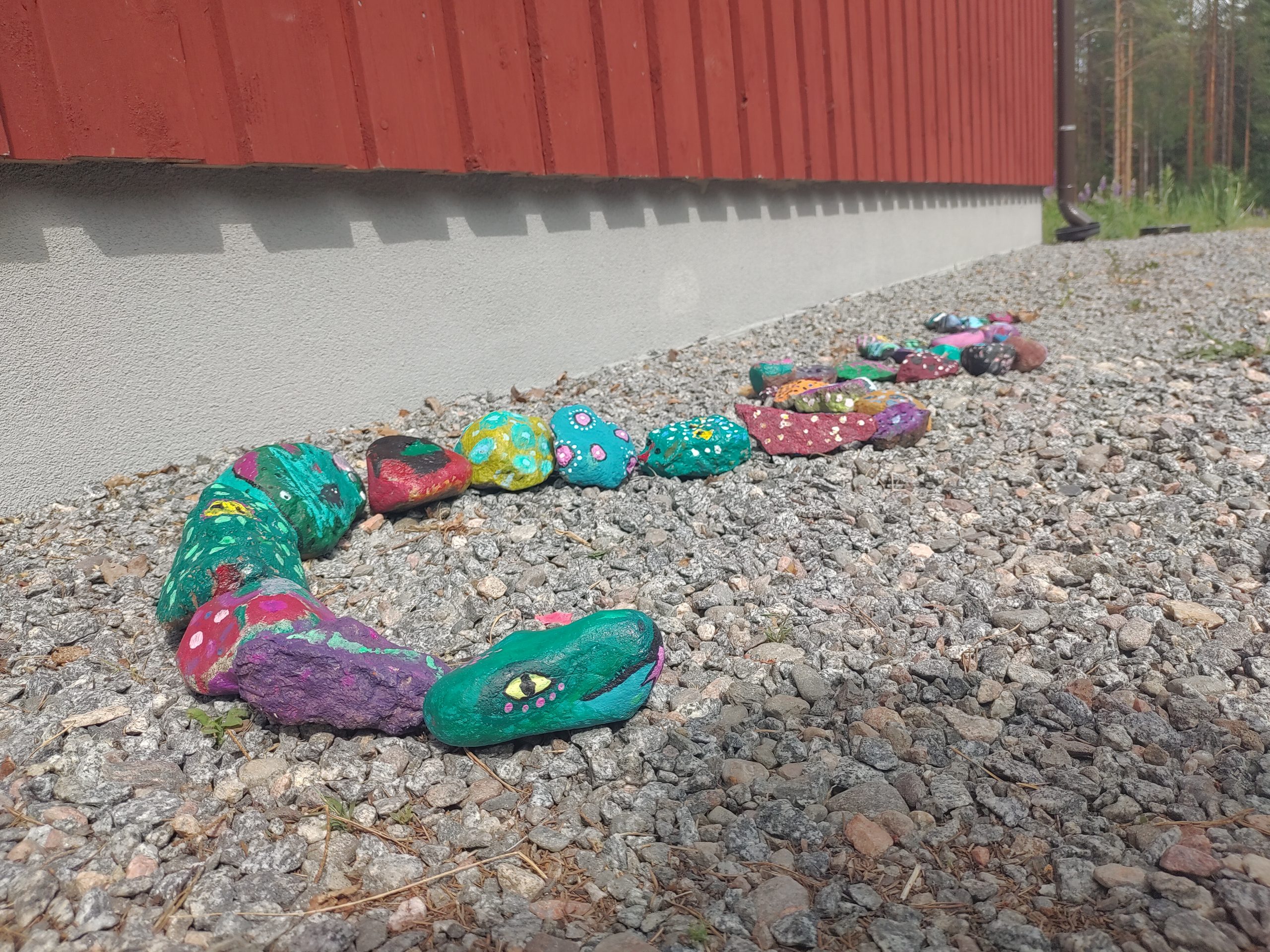 Maalattuja väriokkäitä kiviä aseteltuna käärmeen muotoiseksi.
