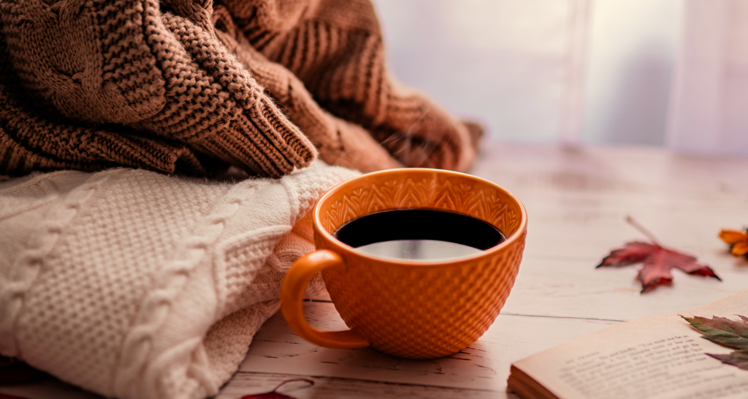 Oranssi kahvikuppi , neule ja kirja pöydällä.